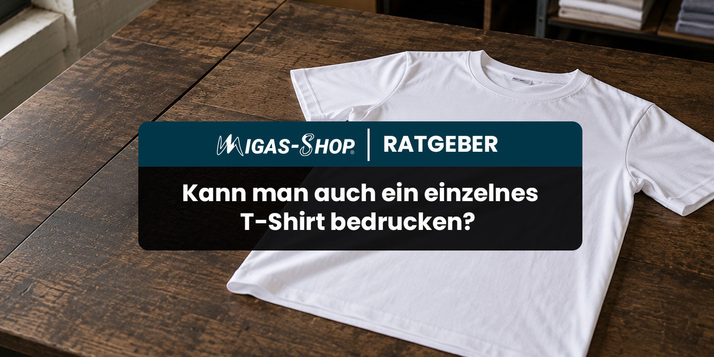 Ausgebreitetes weißes T-Shirt auf rustikalem Holztisch, darüber Banner „MIGAS-SHOP Ratgeber – Kann man auch ein einzelnes T-Shirt bedrucken?"